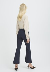 Pantalones acampanados de color marino, hechos de tejido ligero, con una cintura media y bolsillos traseros. Combinados con una blusa de manga larga beige.