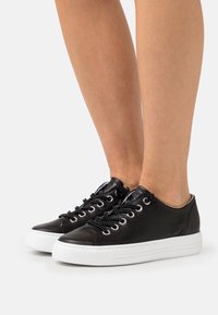 Black leather sneakers with white rubber soles, featuring round laces and metallic eyelets, smooth texture, and a low-top design.