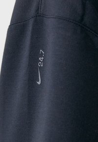 Mikina Nike v tmavě námořnické barvě s hladkou texturou; obsahuje stříbrné logo a tisk "24.7" na rukávu.