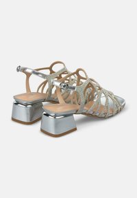 Sandalias de tacón plateado con un diseño de tiras entrecruzadas, adornadas con estrás transparentes, que cuentan con un tacón cuadrado y una plantilla beige.