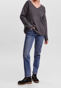 Maglione oversize a collo a V di colore grigio scuro; jeans blu a gamba dritta; stivali in camoscio nero con dettagli in pizzo e suole in gomma color cuoio.