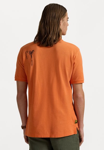 Oranje polo shirt met korte mouwen van textuurstof. Bevat zwarte palmboomgraphics op de achterkant en een zijsplit met branding.