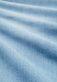 Tissu en denim bleu clair avec une texture de tissage diagonal visible et des plis doux créant des ombres délicates.