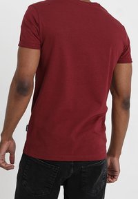 Mörkröd t-shirt med kort ärm i mjuk bomull, med en klassisk rundad halsringning och rak nederkant, samt en liten etikett på vänster sida.