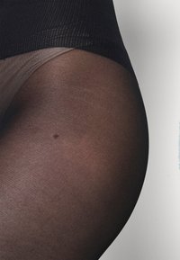 Černé průsvitné punčochy s žebrovaným pasem, které vykazují hladkou texturu a mírný lesk, přecházející od neprůhledného k průsvitnému.