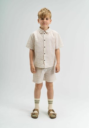 Korte mouwen overhemd met knopen en korte broek in crème met lichtbruine verticale strepen. Gecombineerd met bruine sandalen en crème sokken met groene strepen.