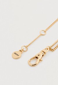 Zelta ķēdes kaklarota ar omāru sprādzi un apaļu piekariņu, uz kura ir iegravēts "DKNY" uz gaiša fona.