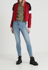 Punane ja must lukuga jakk valgete triipudega, oliiviroheline särk, helesinised kitsaste teksade püksid ja mustad nööbiga ankle saapad.