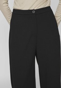 Pantalons noirs ajustés avec une texture lisse, dotés d'une fermeture à bouton à l'avant, de jambes larges et d'un design taille haute.