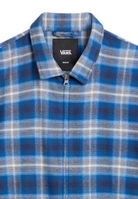 Chemise zippée à carreaux bleu, gris et blanc avec col et étiquette de marque Vans de taille moyenne visible à l'intérieur du col.