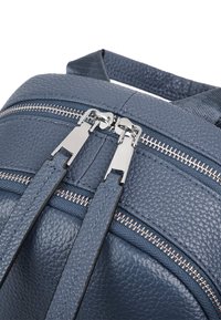 Ciemnoniebieski plecak ze strukturalnej skóry z podwójnymi srebrnymi suwakami i materiałowymi ramiączkami. Wyróżniające się detale to gładka prowadnica suwaka.