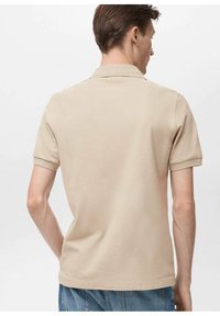 Beige polo-shirt, kortærmet, tekstureret stof, klassisk krave, rene linjer, bæres med blå jeans, simpelt design. Ingen synlig branding.