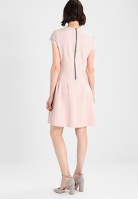 Kurzes, kurzärmliges Kleid aus weichem rosa Stoff mit strukturierten Streifen und einem Reißverschluss auf der Rückseite. Kombiniert mit grauen High Heels.