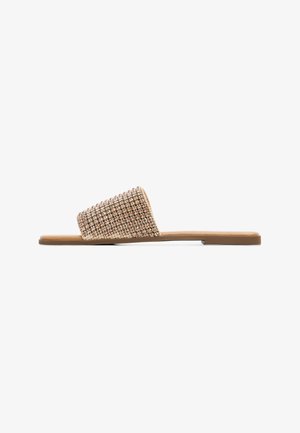Sandale à glissière tissée avec une sangle texturée en rose doré métallique et une semelle plate marron, arborant un design minimaliste et une silhouette ouverte.