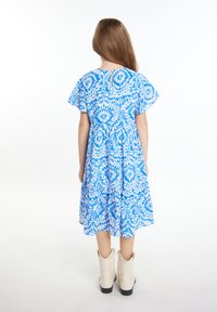 Mėlynos ir baltos spalvų gėlėmis dekoruota suknelė su trumpomis plazdančiomis rankovėmis, prisiūtu liemeniu ir platėjančia sijona. Derinama su baltais kaubojiškais batais.