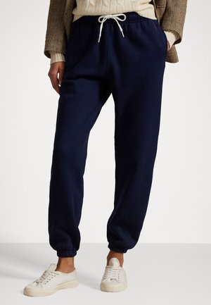Pantalons de survêtement bleu marine en tissu doux avec des poignets élastiques, dotés d'une taille avec cordon de serrage et de poches latérales, associés à des baskets en toile blanches.