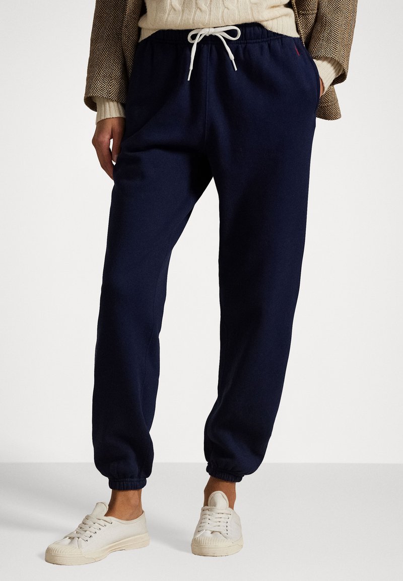 Navy blue sweatpants in soft fabric with elastic cuffs, featuring a drawstring waist and side pockets, paired with white canvas sneakers.