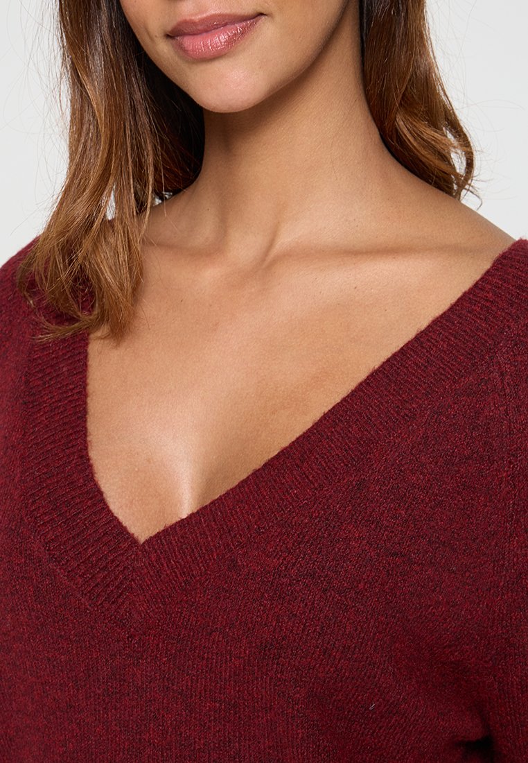 Pull à col en V bordeaux en tissu tricoté doux, avec une coupe décontractée et des détails côtelés au niveau du col et de l'ourlet.