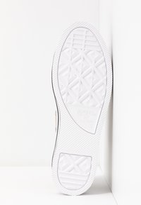 Hvid sål til gummisko med mønstret slidbane, der har et tekstureret design og præget branding. Glatte, afrundede kanter med minimale detaljer.