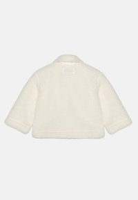 Kreemjas faux-põlvikust jakk, millel on krae, pikad varrukad ja lühike lõige; sisaldab tekstuurset kangast ja lihtsat disaini ilma nähtava riistvarata.