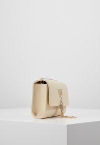 Beige leather handbag with a structured shape, featuring a gold-tone chain strap and decorative hardware on the front flap. Textured finish.