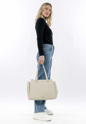 Borsa in pelle beige con un design strutturato, doppi manici superiori e chiusura a zip, tenuta da una persona in jeans blu casual e sneakers bianche.