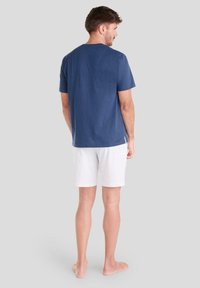 Camiseta de algodón azul marino de manga corta, combinada con pantalones cortos blancos con un estampado de pequeños puntos rojos. Costuras visibles y aberturas laterales.