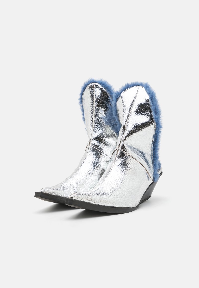Silver cowboy-stil stövlar med en glänsande, sprucken metallisk finish och blå pälskant längst upp. Tån är spetsig, och klacken är kilformad.