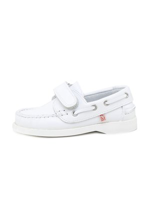 Zapato náutico infantil de cuero blanco con tira de velcro, cordones laterales y un pequeño logo rojo cerca de la suela sobre un fondo blanco.