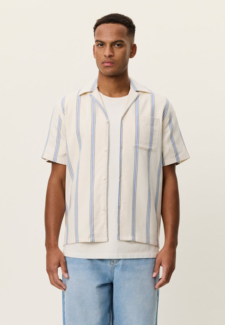 Πουκάμισο με κοντά μανίκια και γιακά σε ανοιχτό μπεζ χρώμα με μπλε ρίγες, κατασκευασμένο από απαλό ύφασμα, με τσέπη στο στήθος και κλείσιμο με κουμπιά μπροστά.