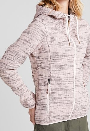 Woman wearing a pink and gray zip-up hoodie with white drawstrings and zip pockets, paired with olive green pants.