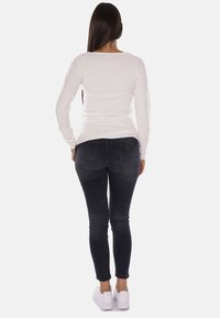 Camicia bianca a maniche lunghe abbinata a jeans skinny scuri e sneaker bianche, vista da dietro, che mette in mostra un design semplice e aderente.