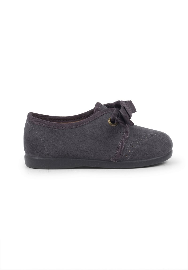 Chaussure en daim gris foncé avec un bout rond et un profil bas. Présente un design à lacets avec un nœud et descoutures décoratives sur la tige.