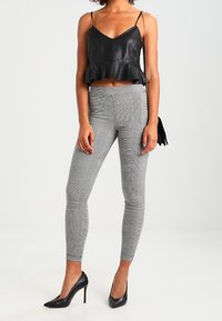 Svart fusk-läder crop top med volangkant, kombinerad med grå rutiga leggings. Modellen bär svarta högklackade skor och minimala accessoarer.