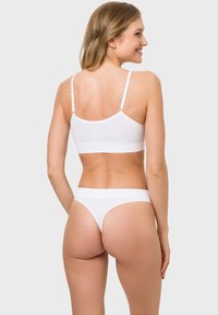 White bralette with adjustable straps and a seamless design, paired with a matching white thong featuring a wide waistband and minimal coverage.
