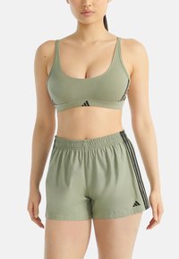Sada sportovního podprsenky a šortek ve světle olivově zelené barvě s černými bočními pruhy. Podprsenka má tenké ramínka a šortky mají elastický pas.