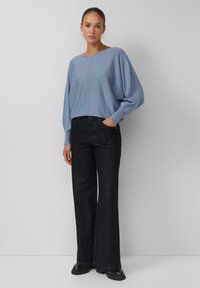 Hellblauer übergroßer Pullover mit rundem Ausschnitt und überschnittenen Schultern, kombiniert mit hoch taillierten schwarzen Schlagjeans. Glatte Textur, minimale Details.