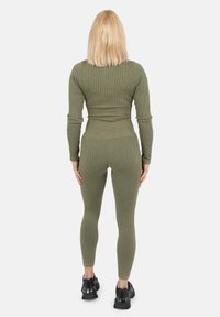 Oliwkowy, prążkowany top z długim rękawem oraz dopasowane legginsy, wykonane z elastycznego materiału, zestawione z czarnymi, masywnymi sneakerami.