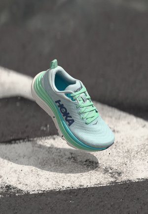 Light blue running shoe with a textured upper, green accents, and white sole. Features laces and a heel tab for easy wear.