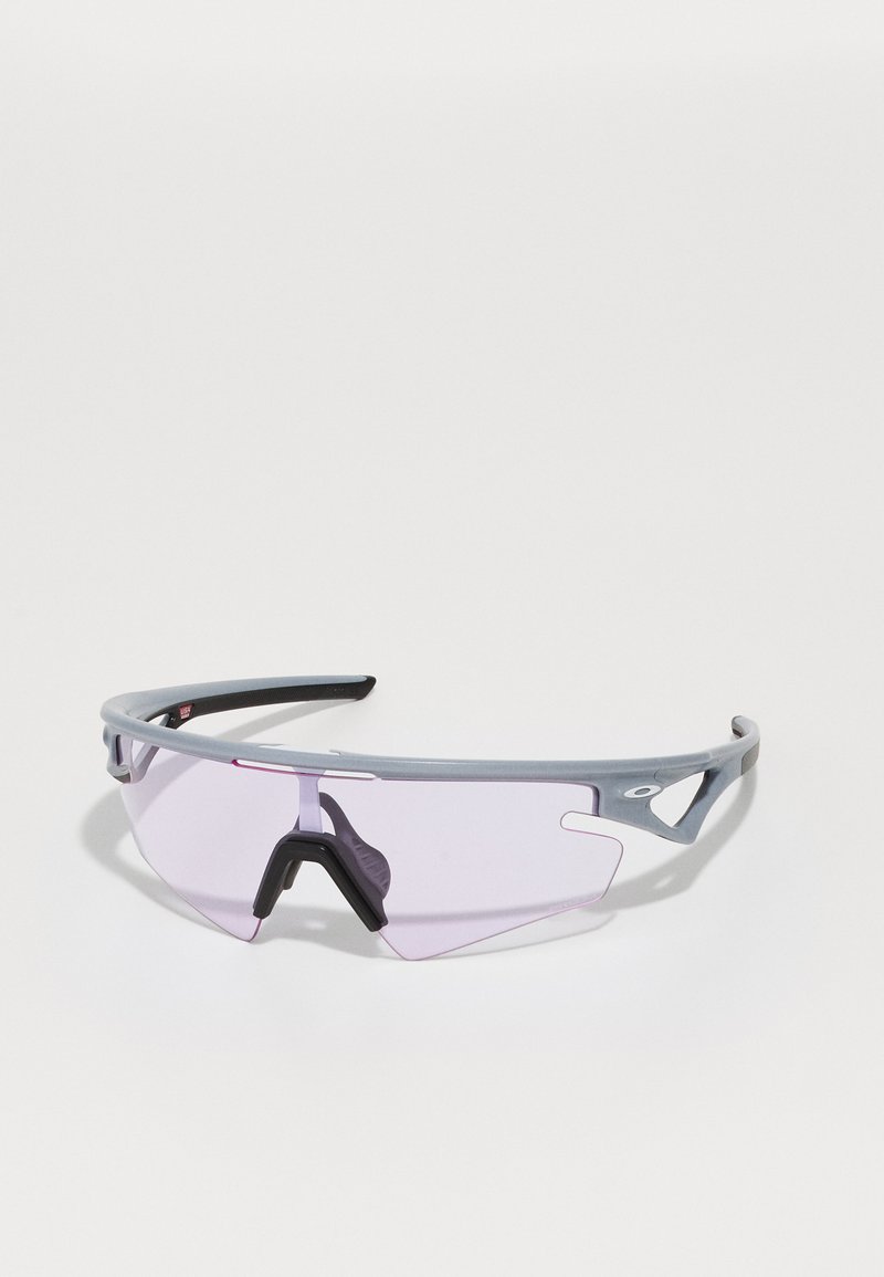 Sportsonnenbrille mit grauem Rahmen, lila getönten Gläsern und schwarzer Nasenauflage. Verfügt über ein schlankes Design und Ausschnitten an den Seiten.