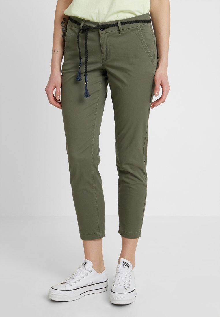 Khaki chinos s úzkým střihem, s pleteným černým pásem, předními kapsami a zkráceným designem. V kombinaci s bílými teniskami.