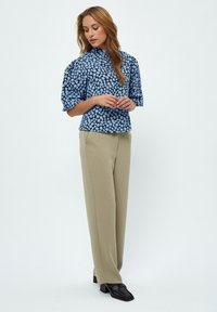 Blusa azzurra a maniche corte con motivo floreale, scollatura alta; abbinata a pantaloni beige a gamba dritta e mocassini neri.