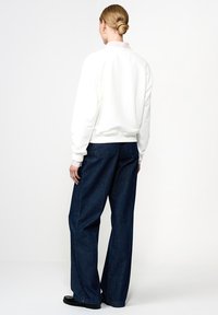 Biała bluza z ribbowanym kołnierzem, w połączeniu z ciemnoniebieskimi szerokimi spodniami dżinsowymi. Gładka faktura, luźny krój i prosty design.
