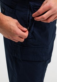 Marine cargoshorts zijn voorzien van een ritszak, meerlagige stiksels en een gestructureerde stof, ideaal voor functionaliteit en comfort.