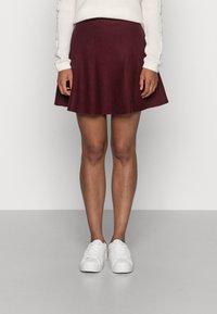 Burgundy flared skirt made of soft fabric, featuring a smooth texture and a mid-length cut, paired with white sneakers.