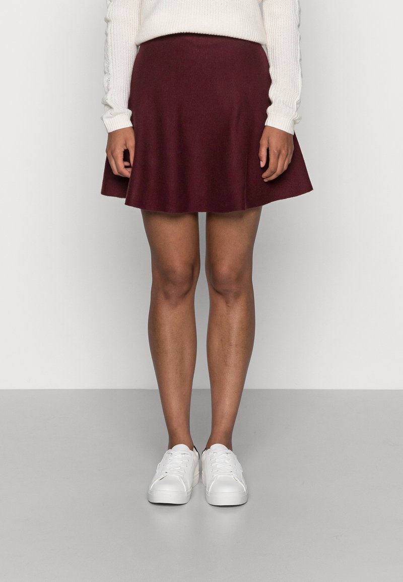 Burgundy flared skirt made of soft fabric, featuring a smooth texture and a mid-length cut, paired with white sneakers.