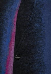Manteau en mélange de laine avec un extérieur bleu foncé agrémenté d'un dégradé de nuances de violet et de rose, terminé par un bouton noir rond et marqué.