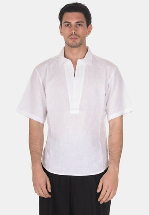 Uomo che indossa una camicia di lino bianca manica corta con scollatura a V, in piedi davanti a uno sfondo bianco uniforme.