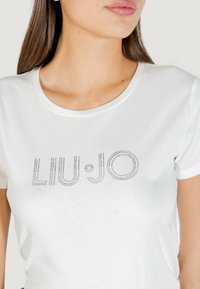 Biały bawełniany t-shirt z logo "LIU•JO" zrobionym ze srebrnych kryształków, o okrągłym dekolcie, krótkich rękawach i gładkiej fakturze.
