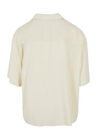 Chemise à manches courtes crème avec une coupe décontractée, col et seam de dos. Tissu lisse avec un léger éclat et sans motifs visibles.